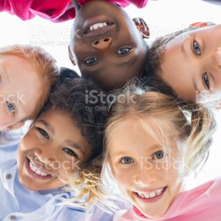 Closeup face of happy multiethnic children embracing each other and smiling at camera. Team of smiling kids embracing together in a circle. Portrait of young boy and pretty girls looking at camera.